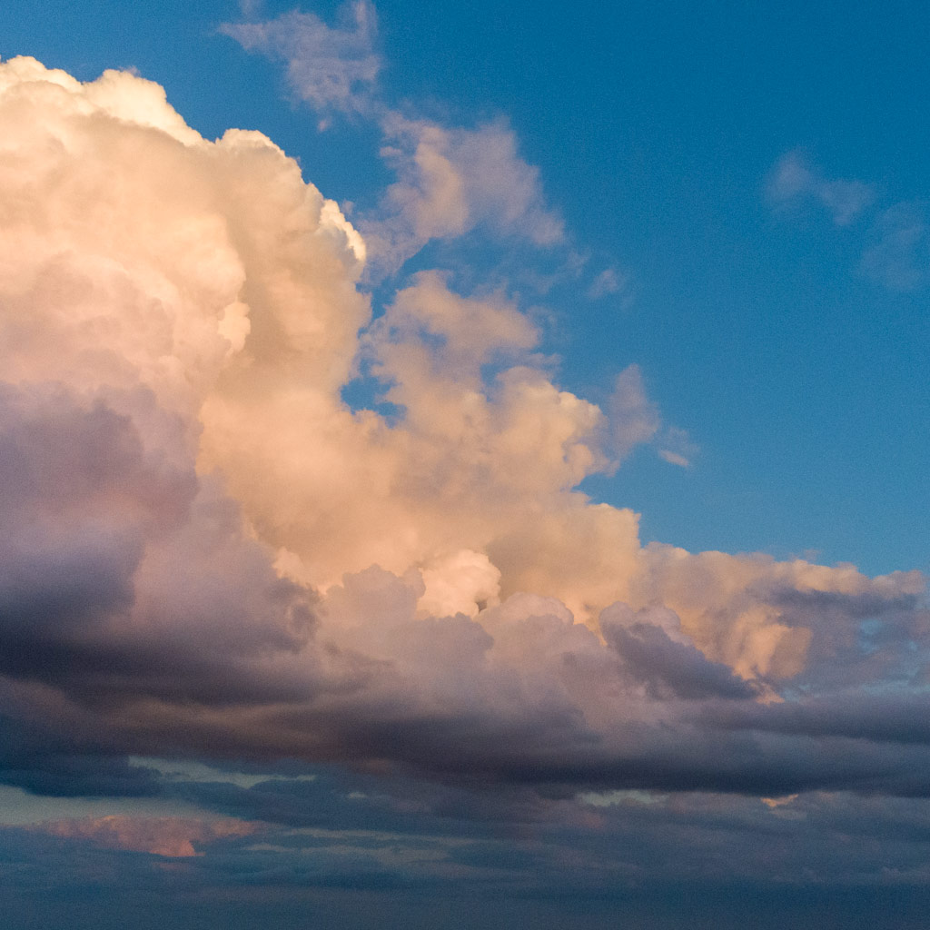 A large, billowing cumulus cloud catches the twilight sun