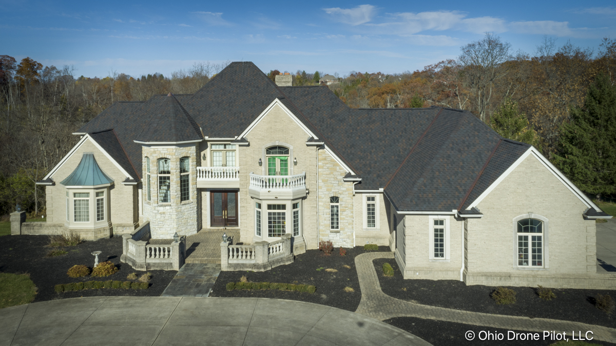 Elevated front view of a large, beautiful home backed by an autumn forest